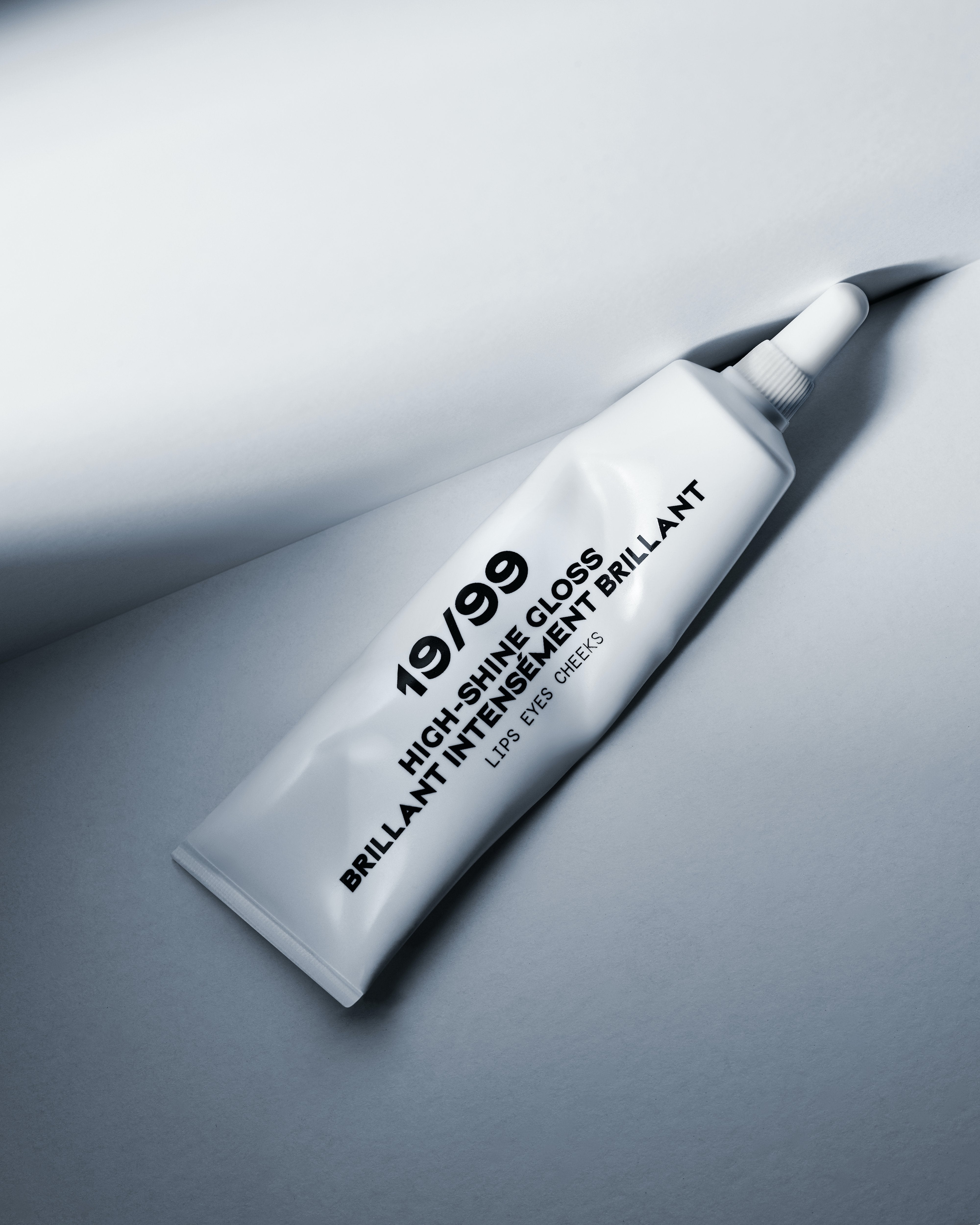 High-Shine Gloss tube, white tube with black text reading '19/99 High-Shine Gloss. Lips, Eyes Cheeks'